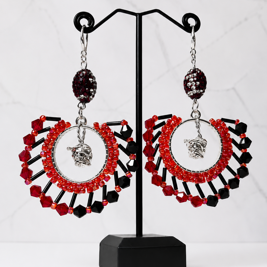 A pair of large statement dangle earrings displayed on a black jewelry stand. The earrings feature red and black faceted beads arranged in a circular fan shape with a silver-toned oval center and a small silver bulldog charm hanging below.