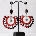 A pair of large statement dangle earrings displayed on a black jewelry stand. The earrings feature red and black faceted beads arranged in a circular fan shape with a silver-toned oval center and a small silver bulldog charm hanging below.